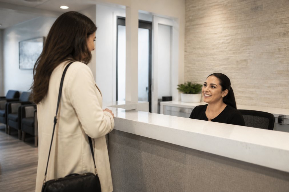 Welcoming modern dental clinic reception area with soft lighting, comfortable seating, and a friendly receptionist greeting a patient at the desk