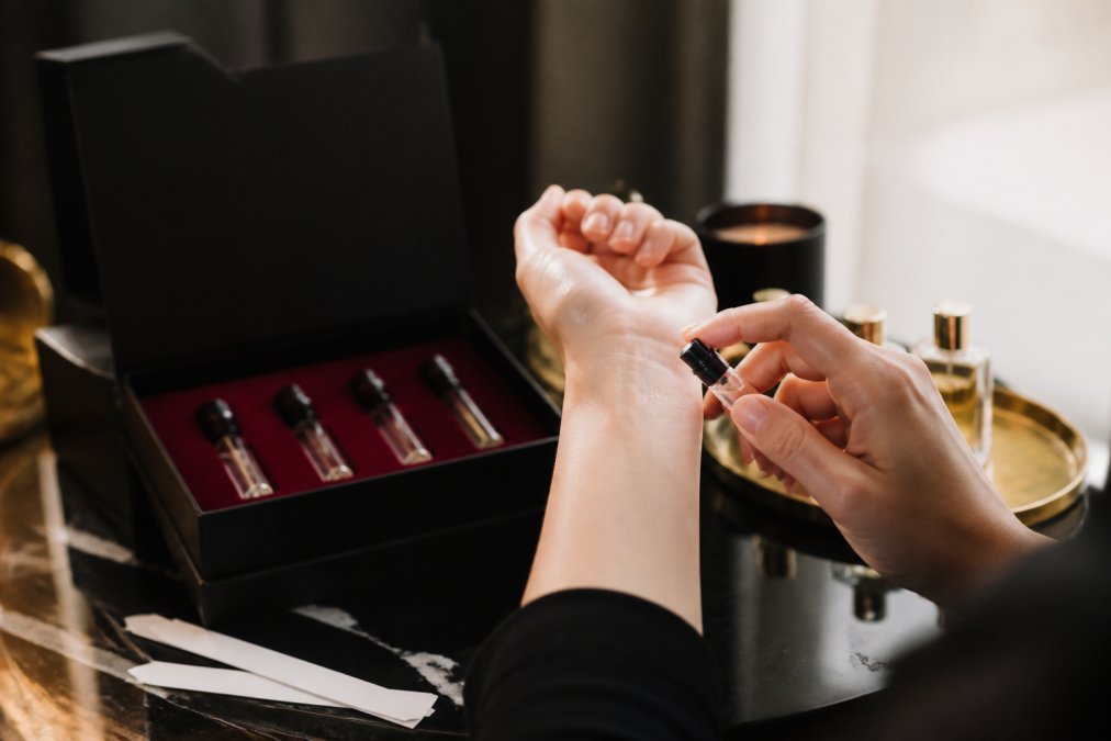 A person applying a vial of sample luxury perfumes to their wrist in natural sunlight