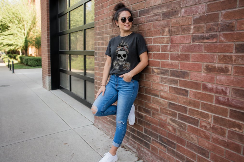Young adult wearing a sarcastic graphic tee styled casually with fitted jeans and white sneakers, posed confidently in natural daylight near a brick wall, showing relaxed everyday confidence