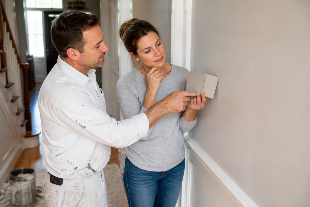Hand holding satin and eggshell paint swatches against a painted hallway wall