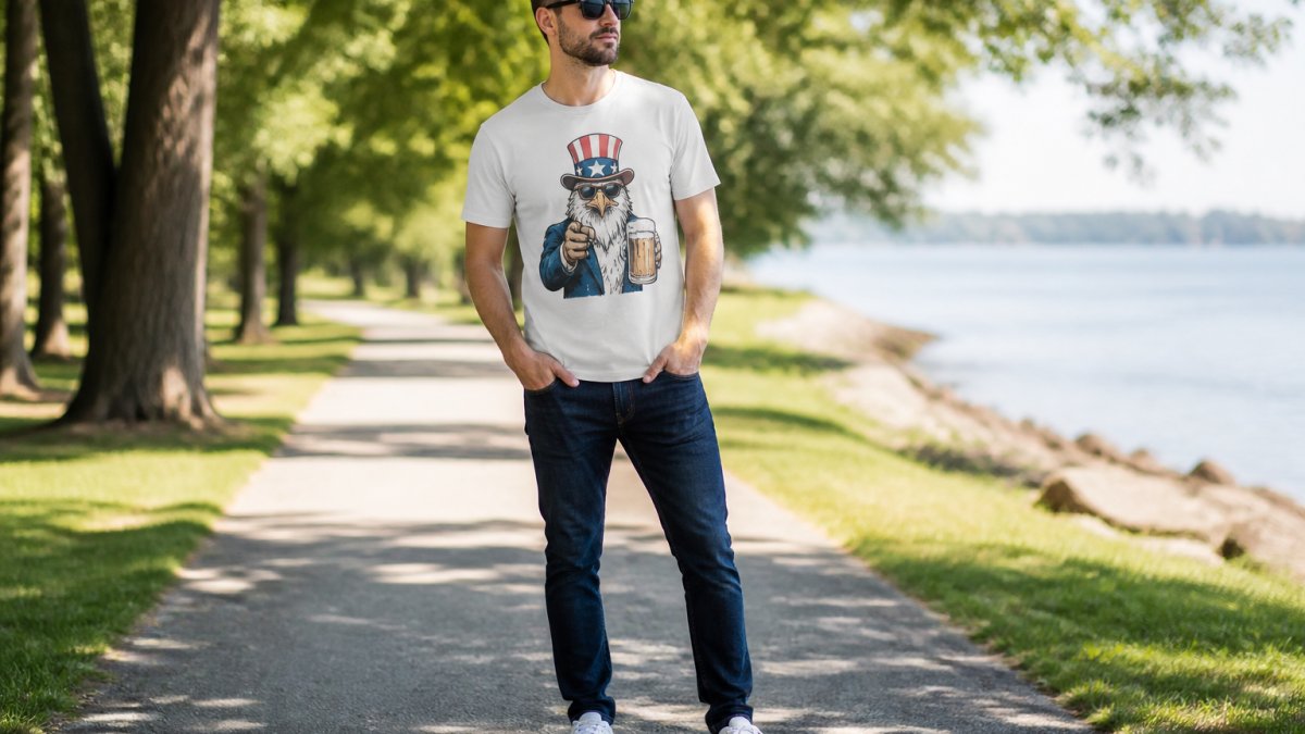 Person wearing a satirical american spirit graphic shirt styled casually with dark jeans and white sneakers, standing in natural outdoor daylight showing the front graphic design clearly visible and shirt fit