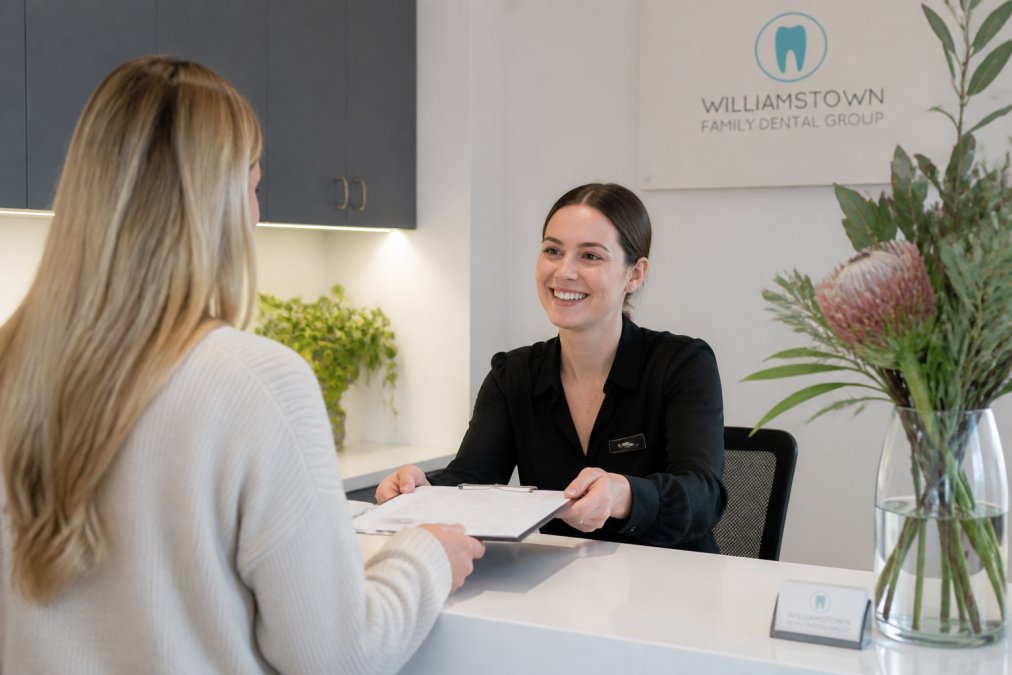 Receptionist assisting a patient at a modern clinic with a Saturday dentist calendar visible on screen