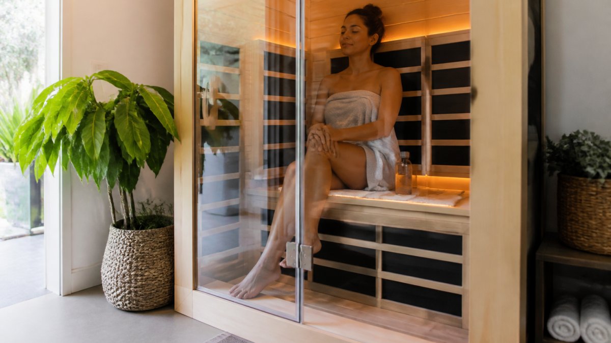 Person relaxing calmly inside a modern wooden infrared sauna cabin with a water bottle nearby
