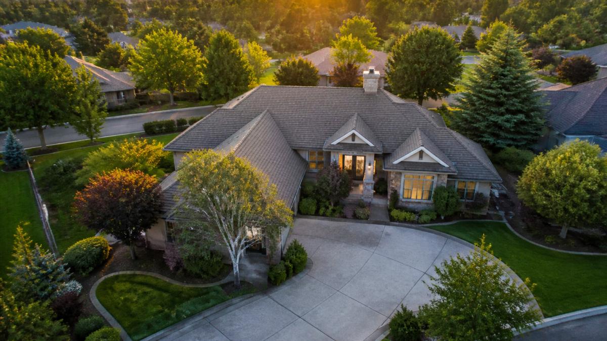 Residential property photographed from aerial perspective during golden hour, showing home architecture, surrounding landscaping, driveway, and neighborhood context from above with warm directional sunlight