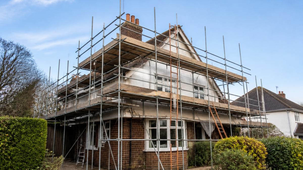 A residential house in Kent with traditional scaffolding erected around the roof and side wall, showing the full scaffold structure against a clear sky