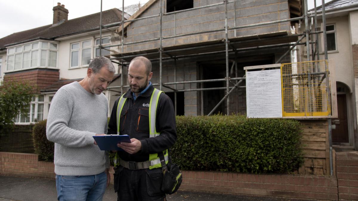 Homeowner and contractor reviewing a scaffolding license notice on a residential extension construction site.