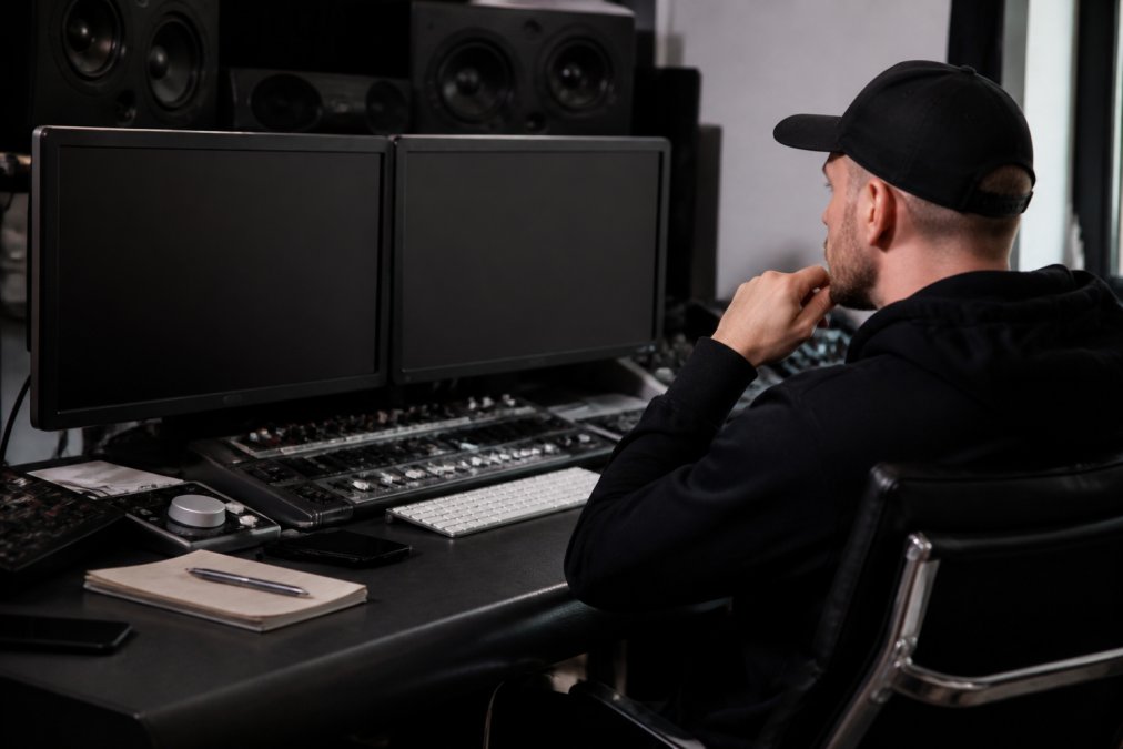 Music producer or label manager reviewing analytics dashboard on multiple monitors in a modern studio workspace, showing colorful waveforms and data charts