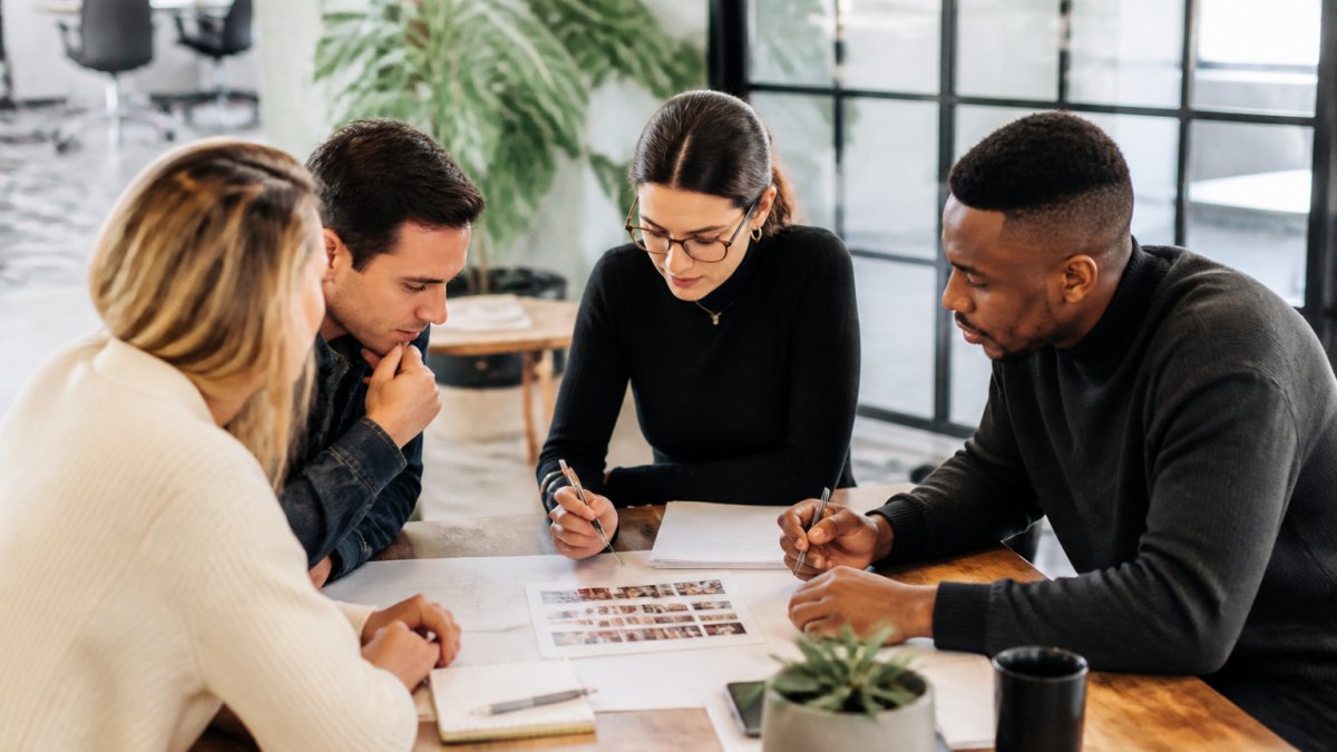 A marketing team gathered around a laptop in a bright modern office, reviewing a list of creator names and outreach notes on screen, natural daylight from large windows