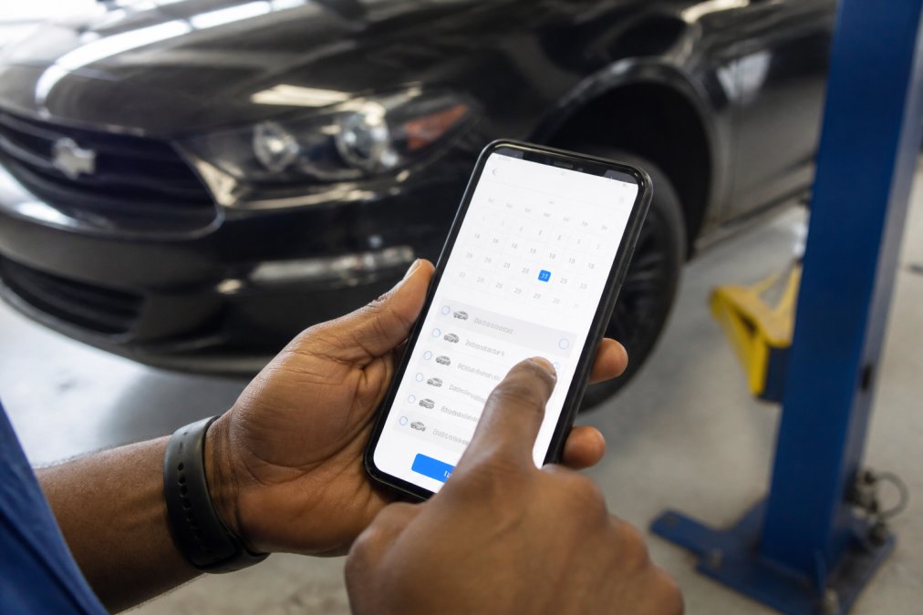 Professional demonstrating schedule same day car repair online technique with hands holding smartphone, tapping through appointment booking interface showing calendar dates and service options on screen