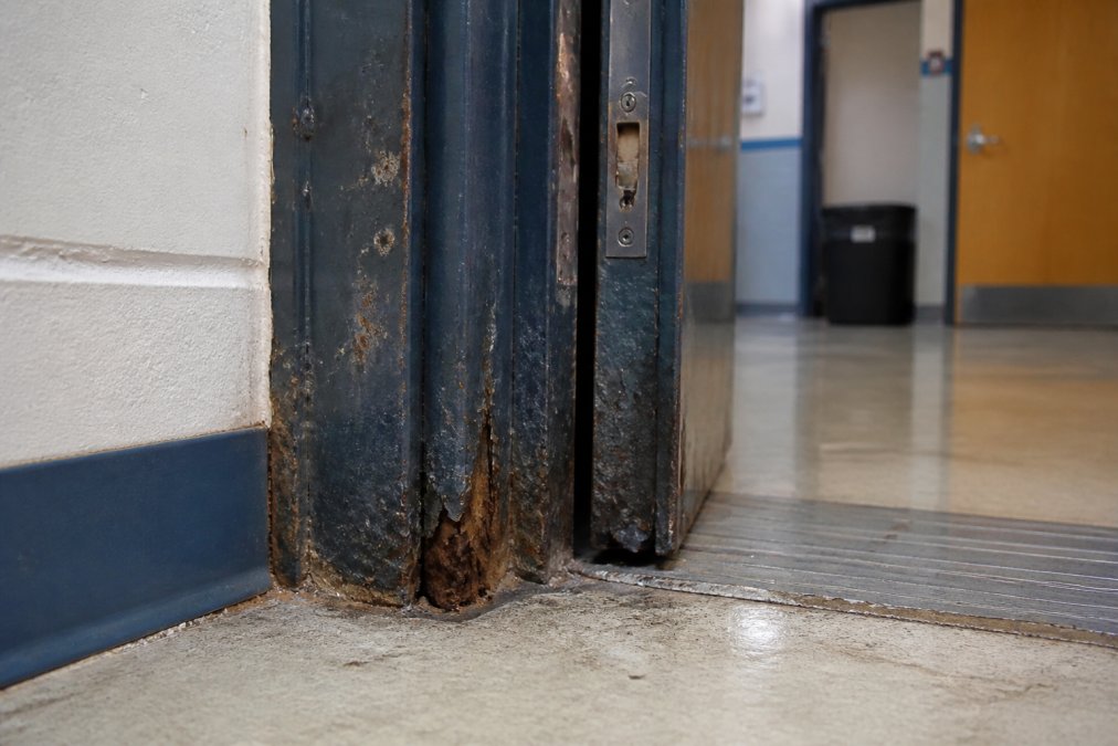 Diagram highlighting rust corrosion and misalignment on a steel school door frame requiring inspection.