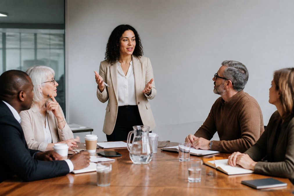 A Scrum Master presenting Agile principles to a group of business stakeholders in a meeting room, with team members engaged and taking notes