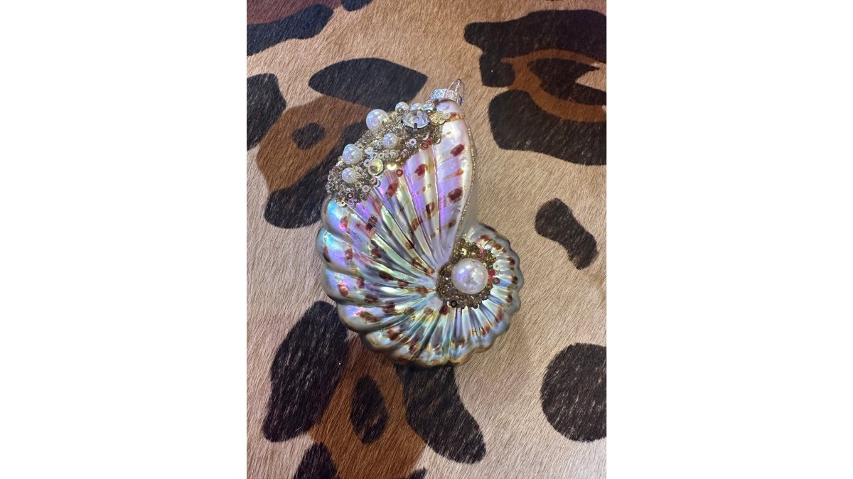 Close-up display of handcrafted jewelry, seashell ornaments, and coastal home decor items arranged on a wooden shelf with natural lighting
