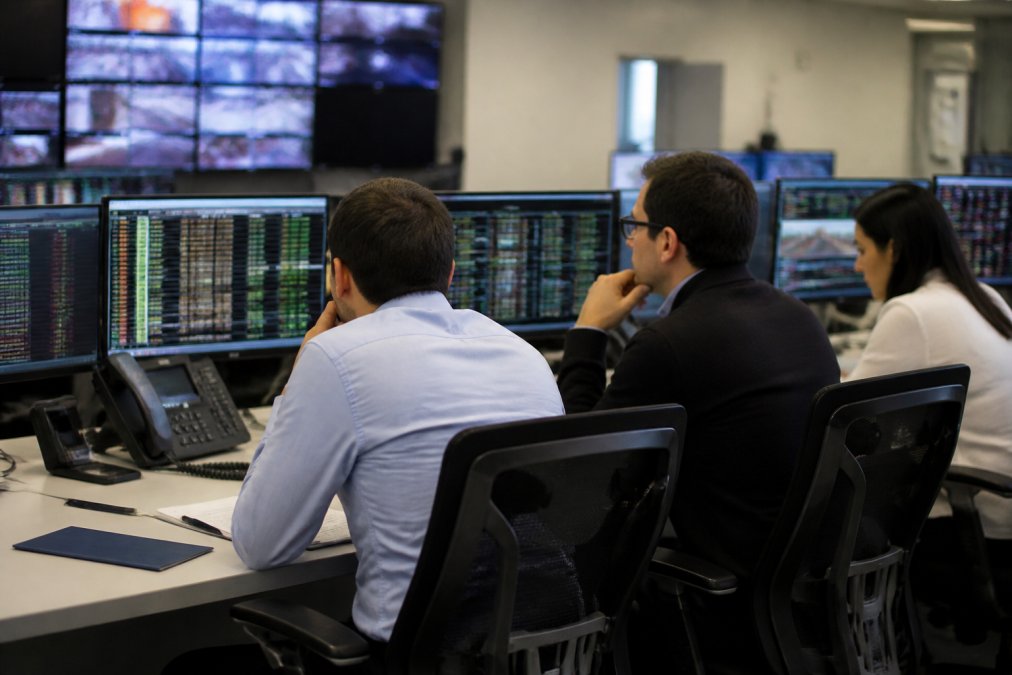 Security team monitoring autonomous agent authorization protocols on multiple screens in a financial operations center, with real-time transaction flows displayed under bright overhead lighting