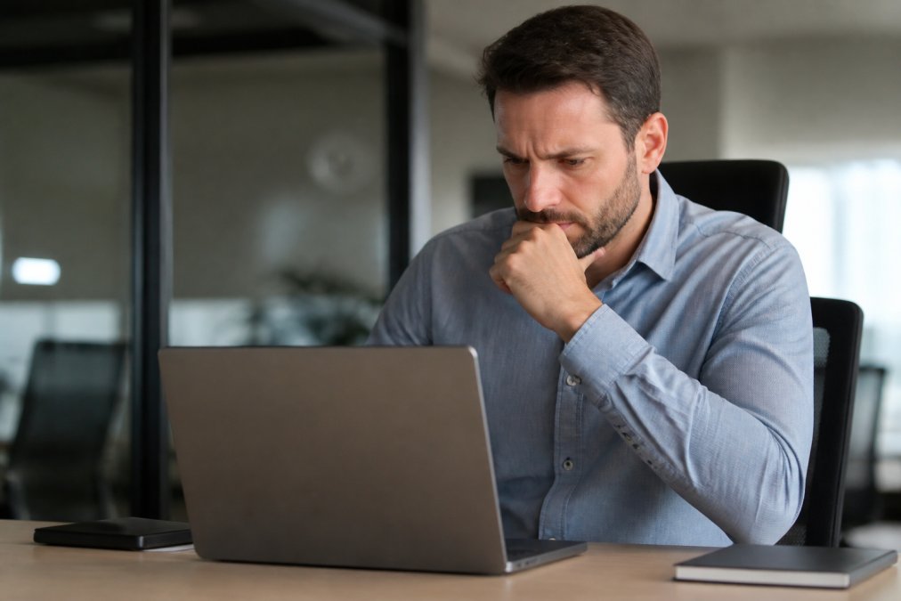 Professional at desk reviewing security warning on laptop screen in modern office, concerned expression visible as they examine browser security notification