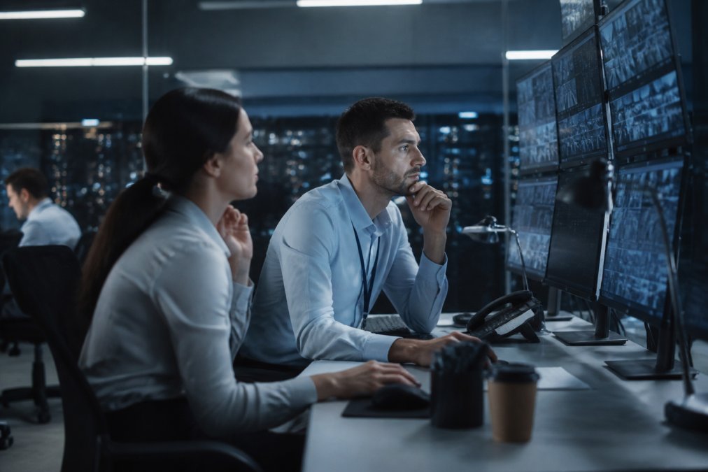 Security team members reviewing authentication logs and digital identity verification screens on multiple monitors in a secure operations center with blue-tinted lighting