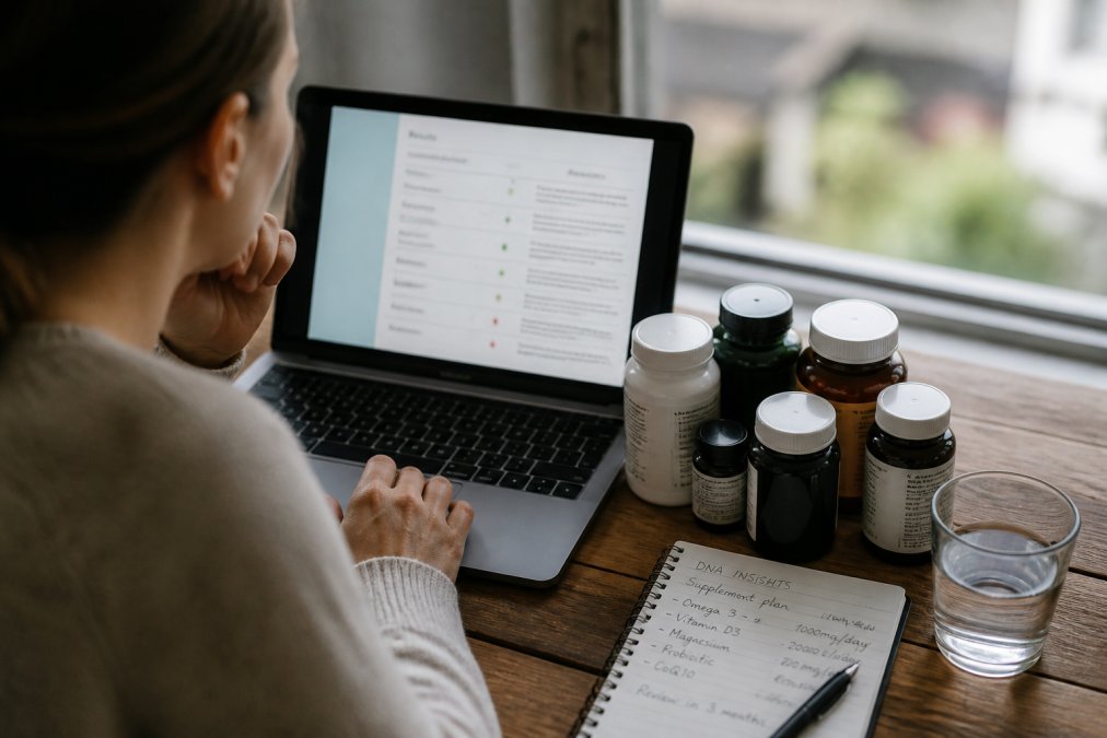 Person reviewing a personalised health report on a laptop, with several supplement bottles and a handwritten notes page showing recommendations visible on the desk beside the computer