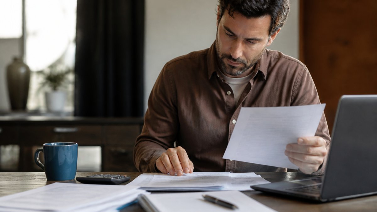 Self-employed professional reviewing property documents and financial records at desk with laptop and coffee, representing the qualification process