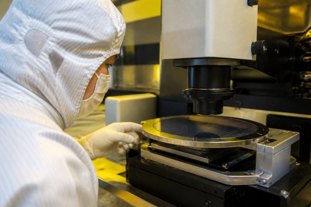 Semiconductor fabrication technician examining wafer samples under advanced inspection equipment in a cleanroom environment with controlled lighting and precision instruments