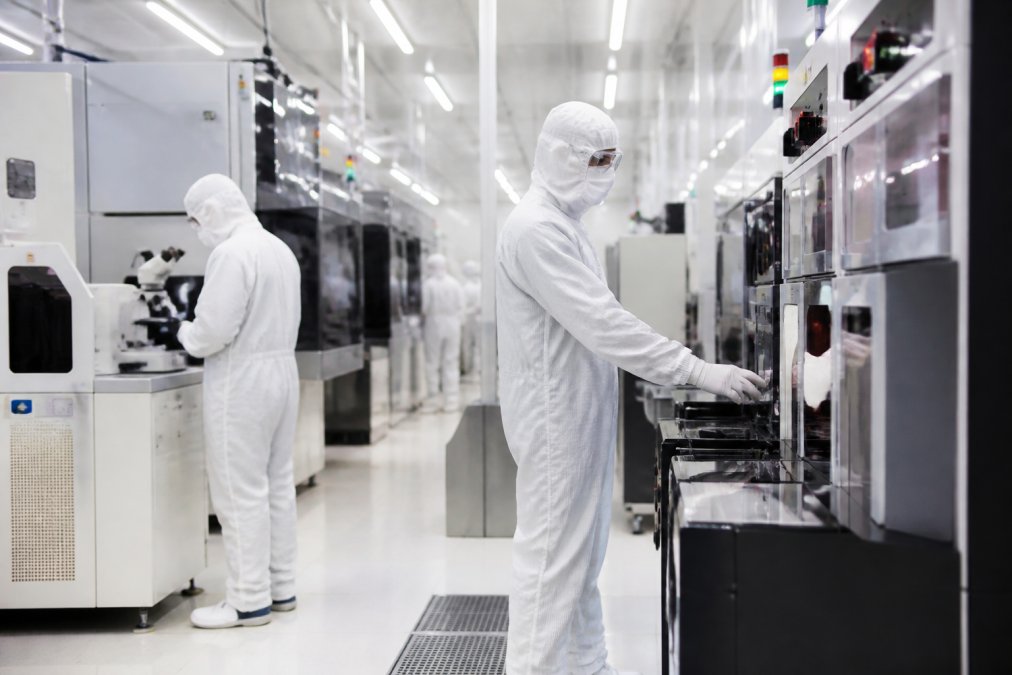 Engineers in full protective gear working inside a semiconductor clean room with advanced equipment and airflow visualization systems in operation