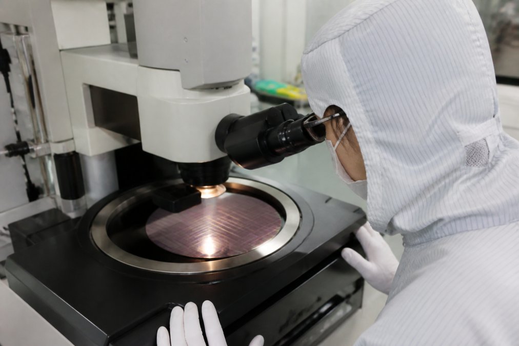 Process engineer examining semiconductor wafer under advanced inspection equipment in cleanroom, with illuminated defect markers visible on wafer surface under precise lighting
