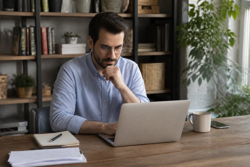 Marketing professional reviewing conversion metrics and lead generation data on laptop at desk with notebook and coffee, focused on analytics work