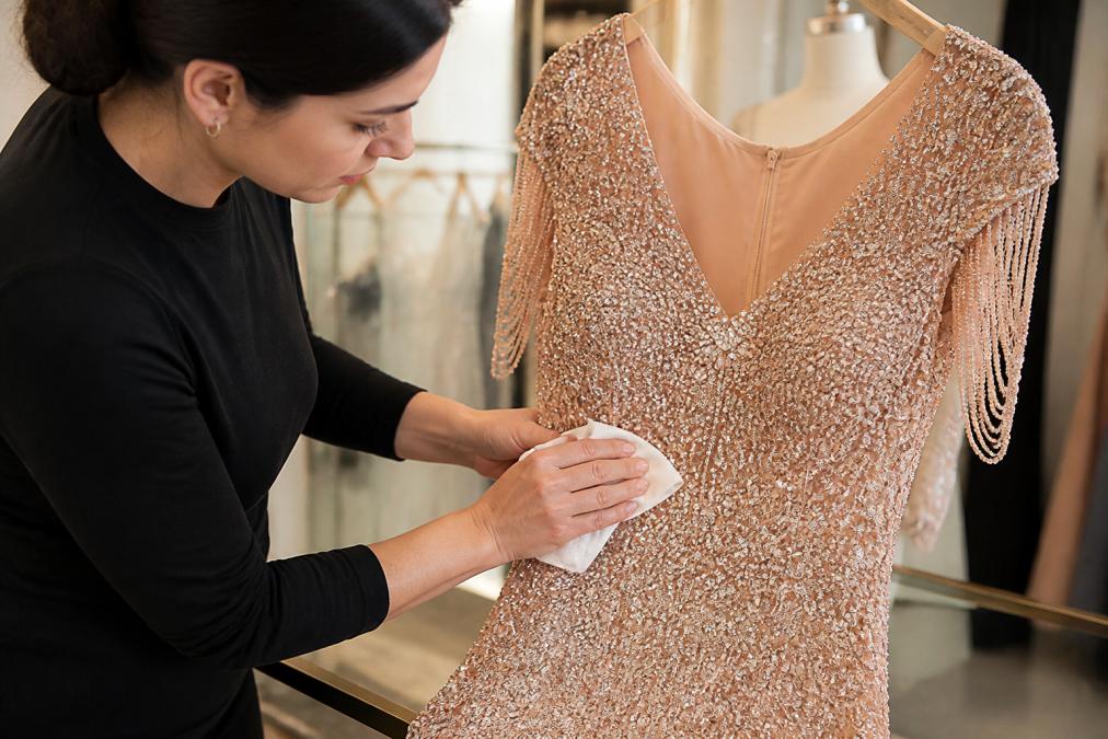 Hands gently handling delicate lace fabric with intricate floral detailing, using a soft white cloth to carefully clean the embroidered areas with light pressure