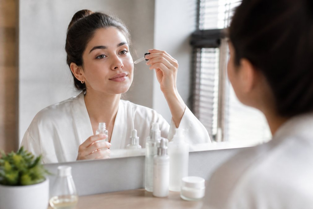 Woman applying facial serum before moisturizer on a bathroom counter