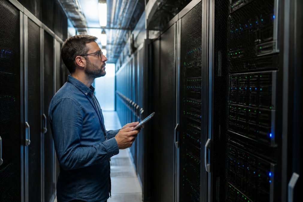 IT manager reviewing server rack status lights in a modern data center aisle, tablet in hand, cool blue lighting