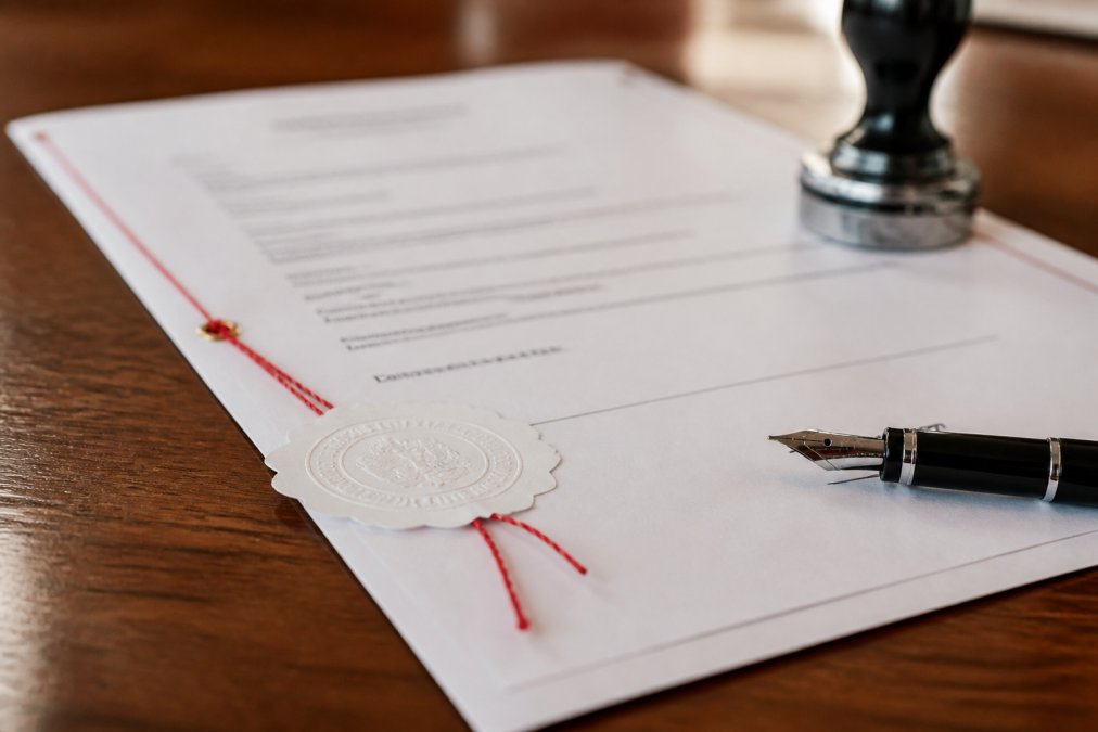 Close-up of a notarized German business document with official seals, red ribbon, and a fountain pen positioned on the signature line