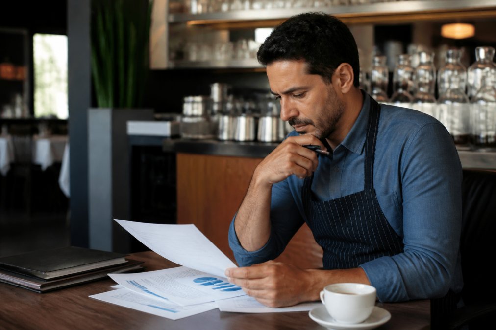 Restaurant manager at a desk reviewing customer data and membership analytics on a laptop screen, focused expression with coffee nearby