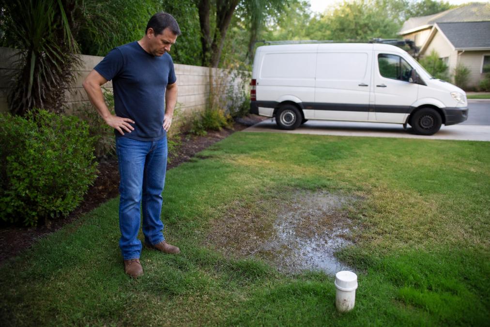 Homeowner inspecting a sunken, wet patch of grass near a cleanout pipe before considering sewer line inspection cost