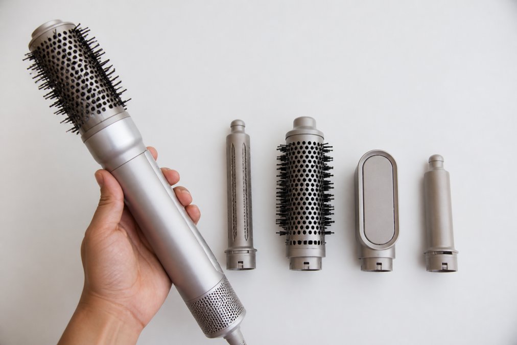 Close-up of the Chaska Air Styler being held in a hand against a neutral white background, showing the device's barrel design, heat plates, and attachment compatibility