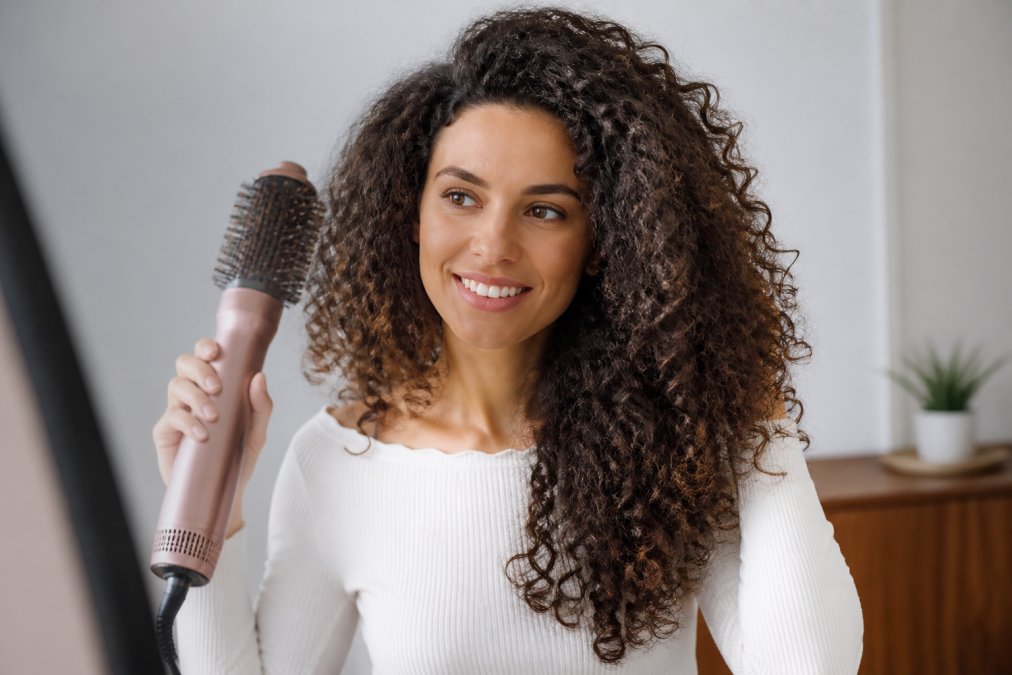 Close-up of a woman with thick, curly hair being styled with a multi-function air styler, showing the finished blowout result with volume and defined curls