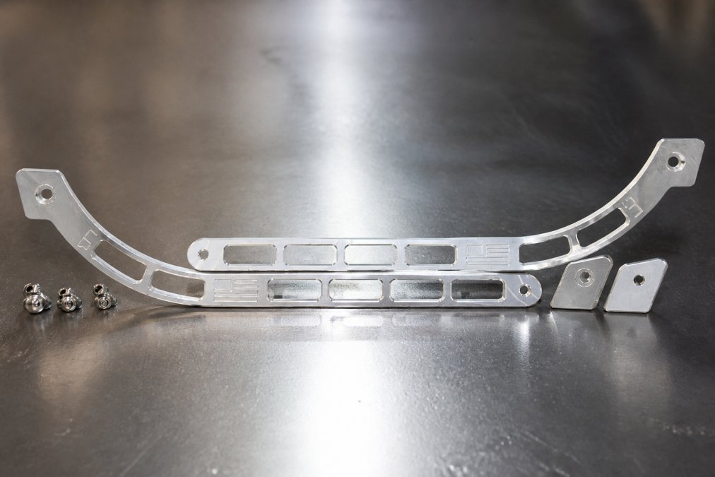 Close-up of precision-machined billet aluminum bracket showing uniform surface finish, symmetrical machine marks, and anodized coating under bright workshop lighting with reflection showing machining quality