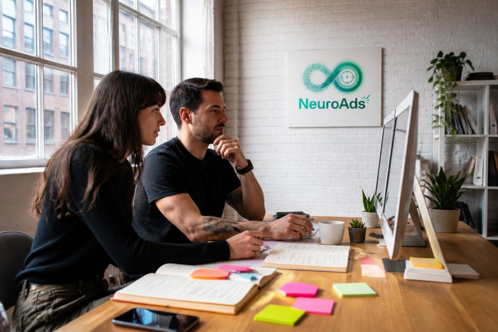 DTC brand founders reviewing Shopify ad automation metrics on dual monitors in a sunlit loft office.
