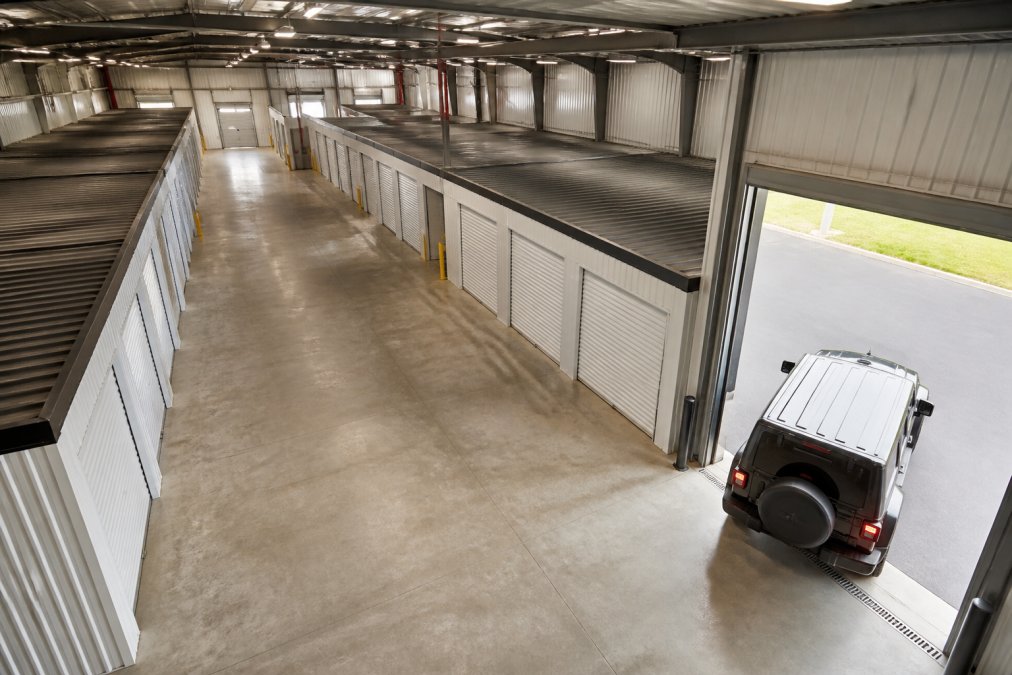 Overhead view of a clean, well-lit indoor vehicle storage facility with rows of secure storage units and a car being pulled into a drive-up access bay