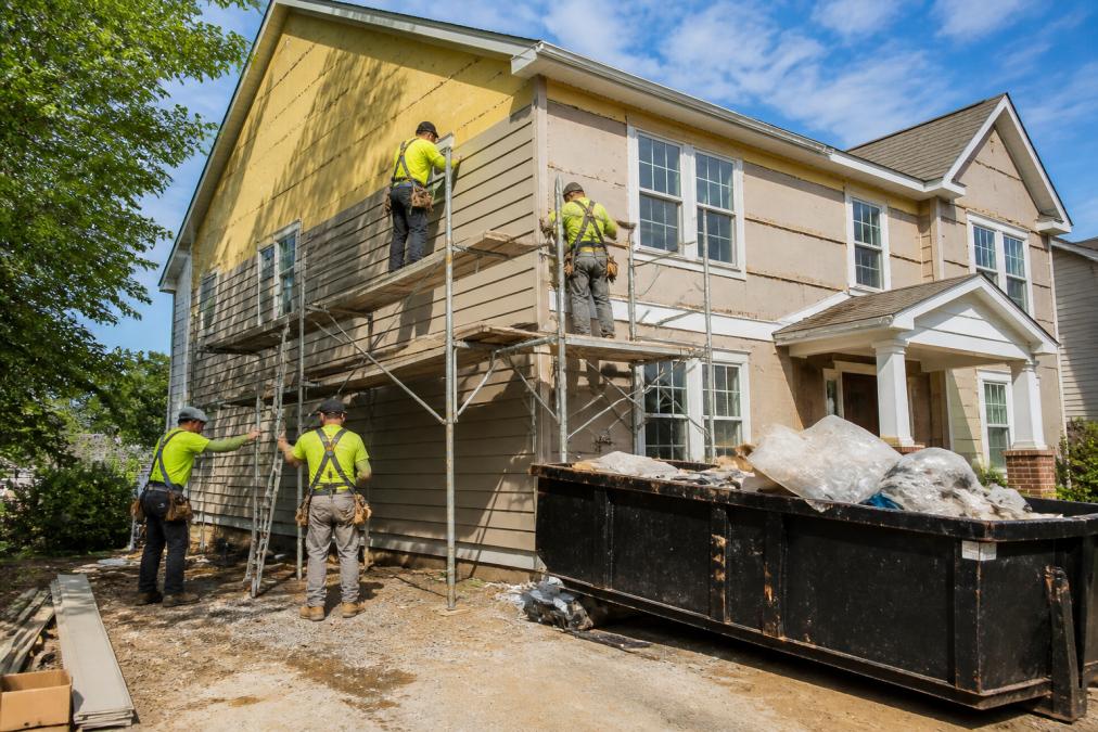 Professional crew performing a siding installation on a two-story suburban home with scaffolding in place.