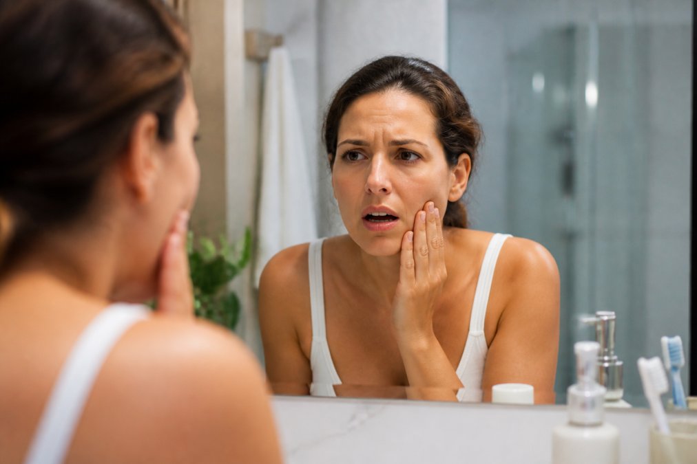 Person in a bathroom mirror holding their jaw in discomfort due to the pain of a cracked tooth