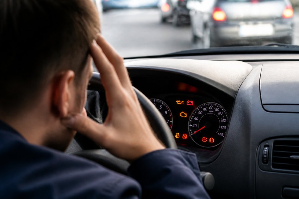 Close-up of a vehicle dashboard with multiple warning lights illuminated in red and yellow, photographed in natural daylight