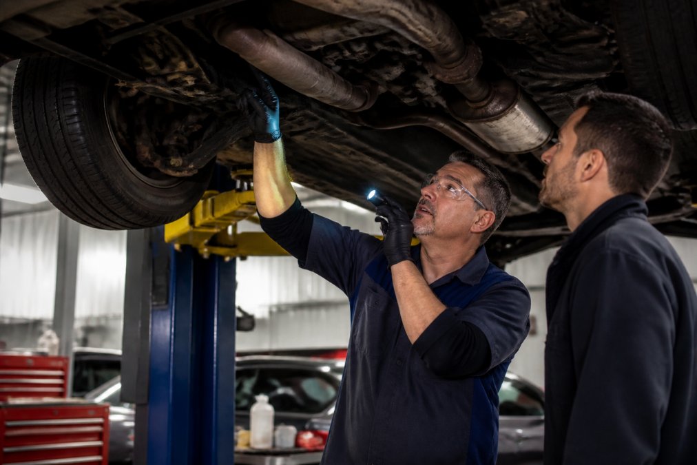 Certified technician inspecting the undercarriage and frame of a used vehicle on a service lift in a professional service bay, with proper lighting