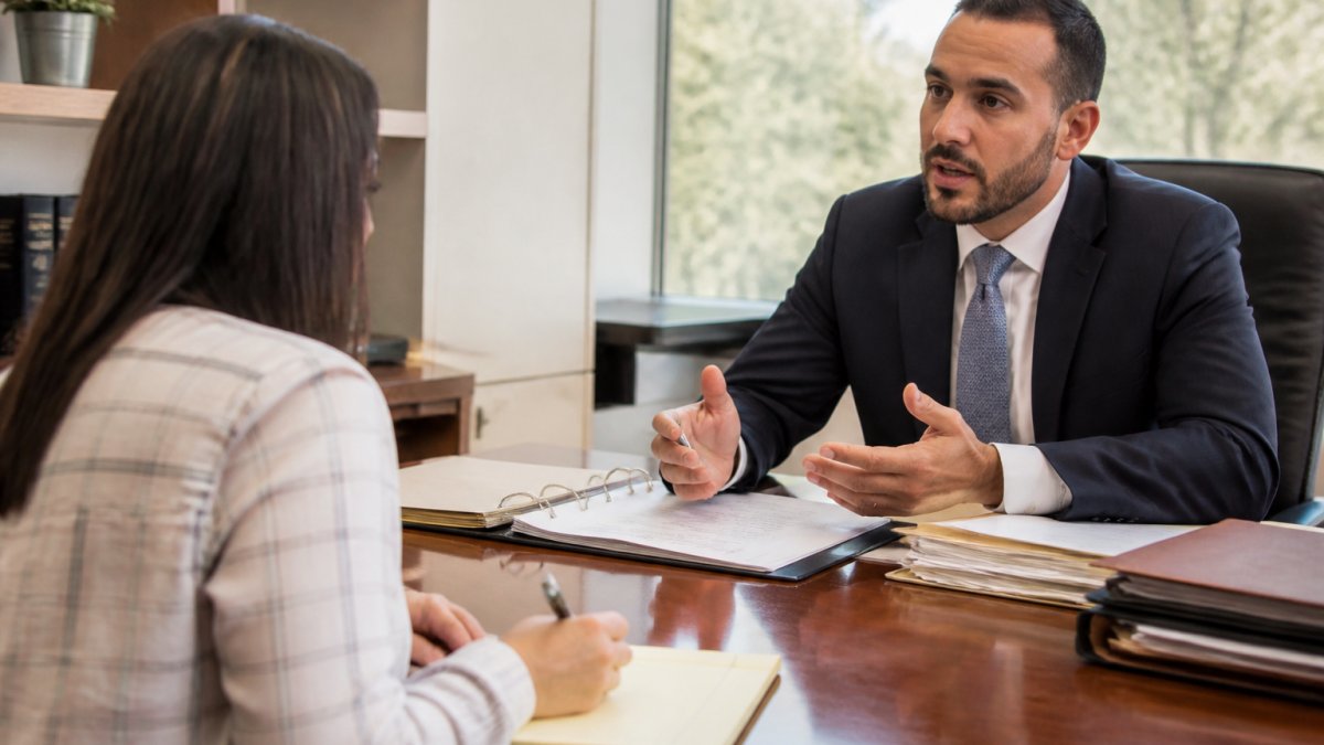Professional immigration attorney meeting with client at desk in modern office, client taking notes with pen and notepad, natural window lighting