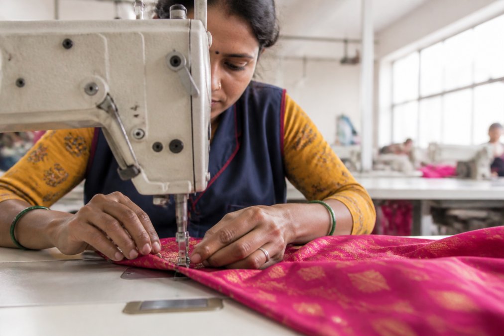 Close-up of a seamstress's hands guiding vibrant fabric through an industrial sewing machine in a bright, clean workshop with natural window light