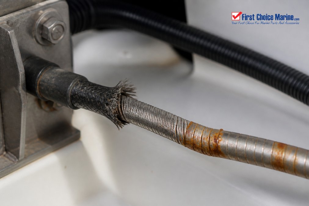 Close-up of a boat steering cable showing visible fraying at the outer conduit, kinking in the metal sheath, and orange corrosion stains on the cable assembly