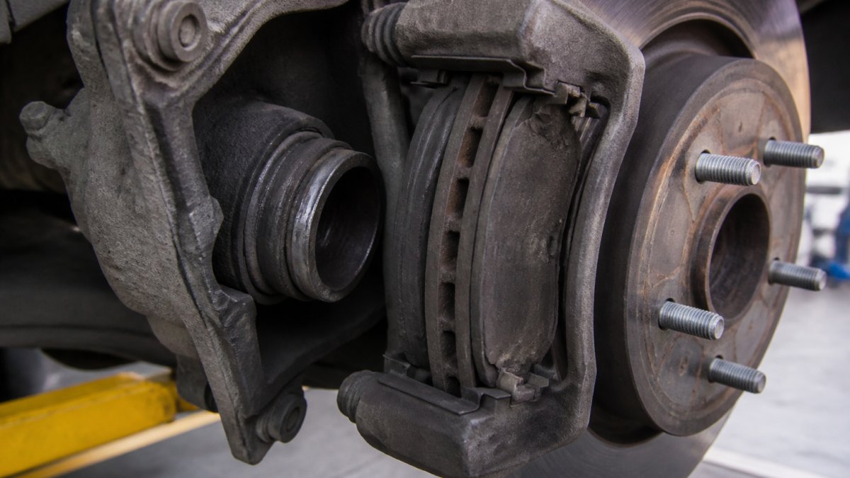 Close-up of brake caliper assembly showing piston, brake pads, rotor with visible dust accumulation and wear patterns on a vehicle wheel