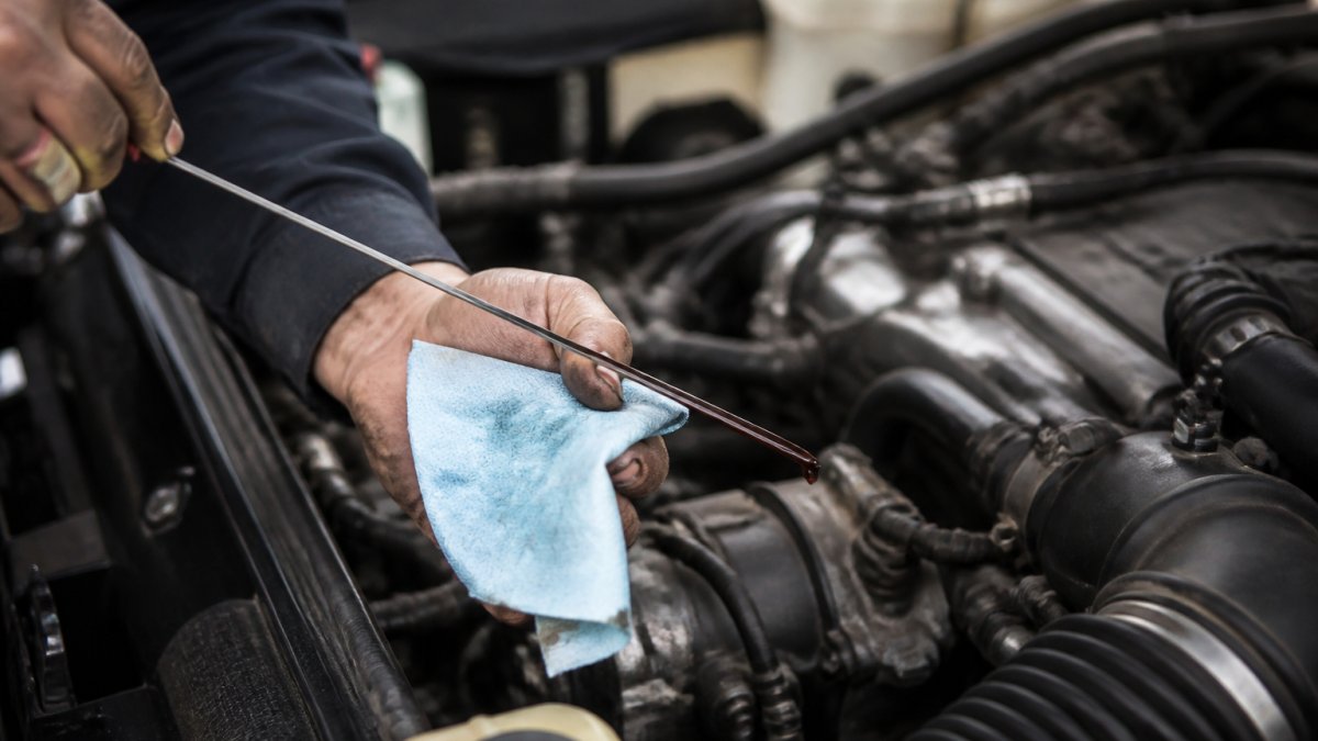 Mechanic's hands checking transmission fluid color and consistency on dipstick in vehicle engine bay