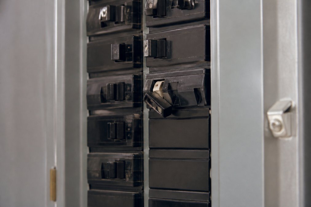 Close-up of a residential electrical panel with multiple circuit breakers, one noticeably tripped to the off position, showing the mechanical switch mechanism clearly