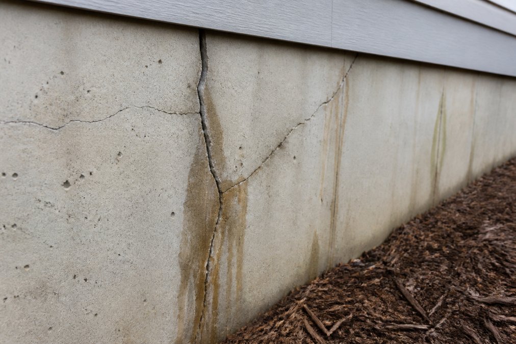 Close-up of foundation wall showing visible hairline cracks running vertically and diagonally through concrete, with water staining visible along crack edges