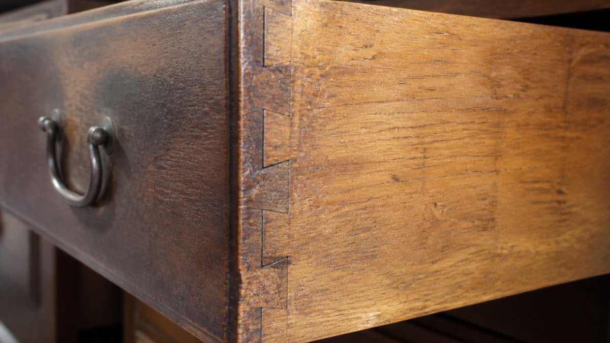 Close-up of a hand-cut dovetail joint on an antique wooden drawer, showing individual wood pieces fitted together with visible saw marks and slightly uneven spacing characteristic of hand craftsmanship