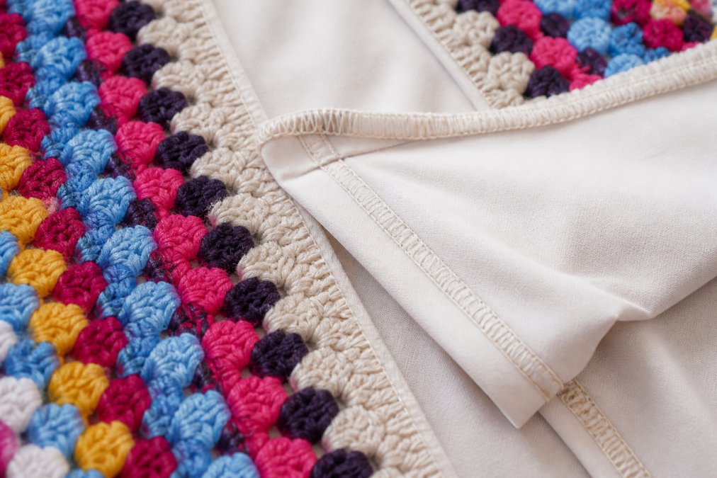 Close-up of a garment's seams showing tight, even stitching with reinforced corners and a serged edge on a cream-colored cotton blouse, photographed in natural daylight