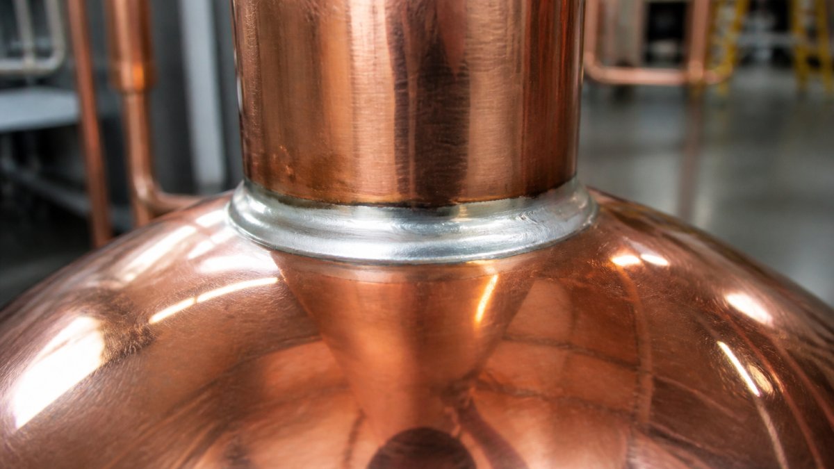 Close-up of copper still solder joints showing clean, uniform silver solder bead with smooth transitions and proper fillet formation, no cracks or voids visible under bright workshop lighting